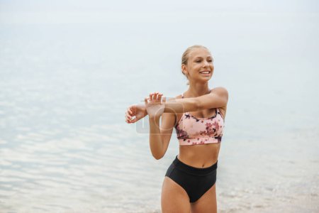 Photo for A beautiful teen girl is doing stretching exercise at the sea beach in summer sunny day. - Royalty Free Image