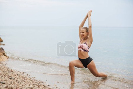 Foto de Una hermosa adolescente está haciendo ejercicio de estiramiento de yoga en la playa del mar en el día de verano. - Imagen libre de derechos