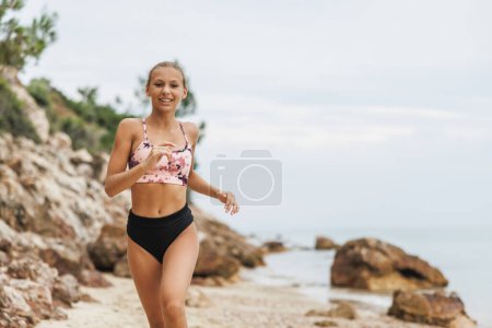 Téléchargez les photos : Adolescente souriante mignonne courant le long de la côte de la mer sur la plage pendant la journée de vacances d'été. - en image libre de droit