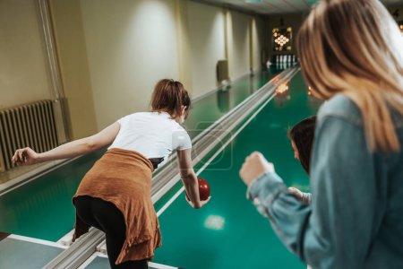 Téléchargez les photos : Rear view of a young woman throwing the bowling ball while her friends are cheering. - en image libre de droit