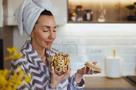 Foto de Retrato de una atractiva mujer disfrutando del olor de sabrosas galletas caseras y teniendo ritual de placer matutino en casa. - Imagen libre de derechos