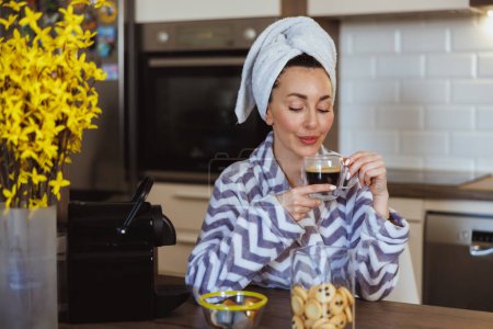 Téléchargez les photos : Jeune femme en peignoir profitant d'une odeur de café savoureux et ayant rituel de plaisir matinal à la maison. - en image libre de droit