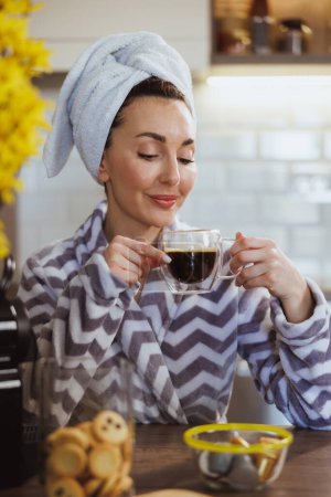 Foto de Una atractiva mujer en albornoz disfrutando del olor a sabroso café y teniendo ritual de placer matutino en casa.. - Imagen libre de derechos