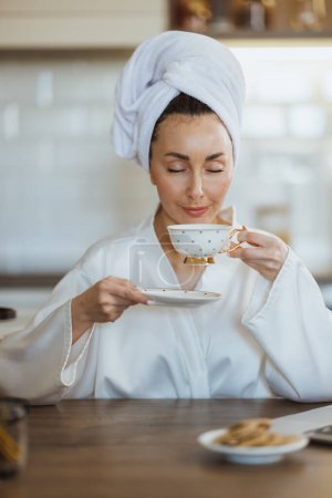 Photo for An attractive woman in bathrobe enjoying of tasty coffee and having morning pleasure ritual at home. - Royalty Free Image