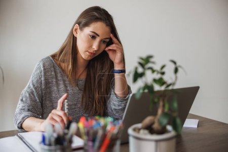 Téléchargez les photos : Jeune femme entrepreneure regardant réfléchi tout en travaillant à partir de son bureau à domicile. - en image libre de droit