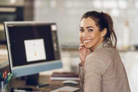 Foto de Retrato de una joven creativa que trabaja en el ordenador en su estudio de casa. Mirando la cámara. - Imagen libre de derechos