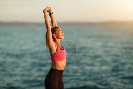 Foto de Feliz joven corredor haciendo ejercicios de calentamiento durante el entrenamiento cerca de la playa de mar. - Imagen libre de derechos