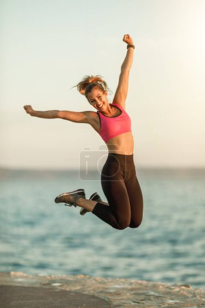 Foto de Joven mujer en forma divirtiéndose y relajándose después de hacer ejercicio cerca del mar. - Imagen libre de derechos