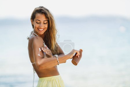 Foto de Una joven atractiva está usando crema de protección solar mientras disfruta en la playa. - Imagen libre de derechos