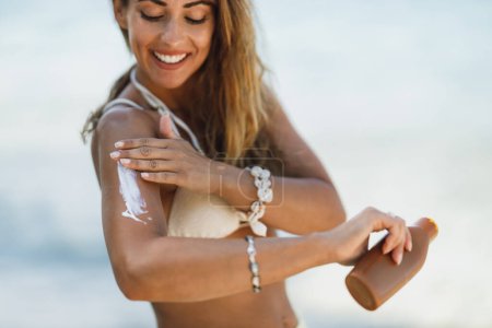 Téléchargez les photos : Prise de vue d'une jeune femme heureuse utilisant une lotion solaire sur la plage. - en image libre de droit