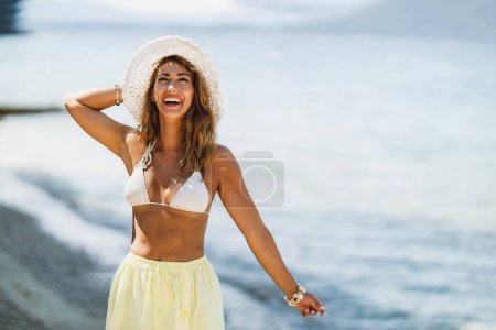 Téléchargez les photos : Une jolie jeune femme en bikini, avec un chapeau d'été, s'amuse sur la plage et profite de vacances d'été. - en image libre de droit