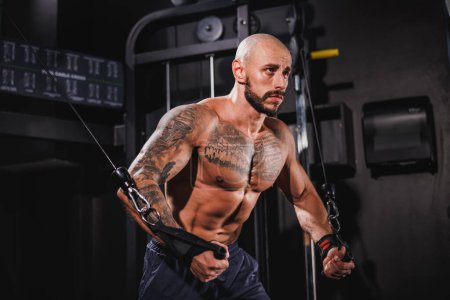 Téléchargez les photos : Un jeune homme de fitness musclé faisant un entraînement dur pour ses muscles de la poitrine sur une machine de gymnastique. - en image libre de droit