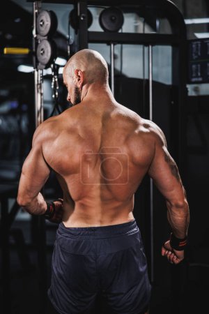 Foto de Vista trasera de un joven musculoso culturista mostrando sus músculos de la espalda perfectos mientras posa después de hacer ejercicio en el gimnasio. - Imagen libre de derechos