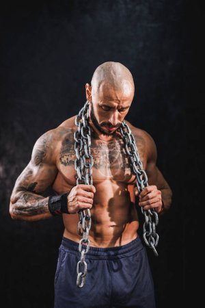 Photo for A young fitness man standing in the gym and preparing to strength training with heavy chain. - Royalty Free Image
