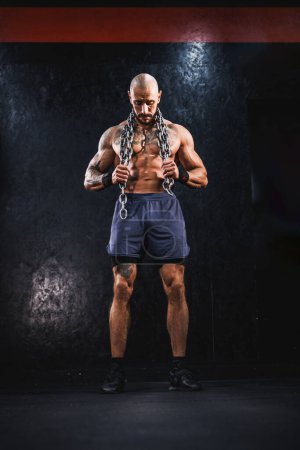 Photo for Shot of a young muscular bodybuilder showing his perfect muscles while posing with chains before work out at the gym. - Royalty Free Image