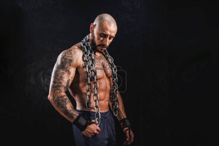 Téléchargez les photos : Prise de vue d'un jeune bodybuilder musculaire montrant ses muscles parfaits tout en posant avec des chaînes avant de travailler à la salle de gym. - en image libre de droit