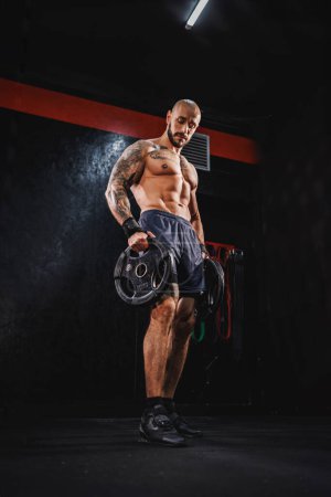 Foto de Tiro de un joven musculoso fitness mostrando sus músculos perfectos después de hacer ejercicio con la placa de peso en el gimnasio. - Imagen libre de derechos