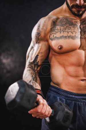 Photo for Closeup shot of a young fitness man exercising with a dumbbell at the gym. He is pumping up his biceps muscle with heavy weight. - Royalty Free Image