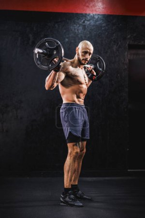 Téléchargez les photos : Prise de vue d'un bodybuilder musclé faisant un entraînement dur avec un haltère pour ses muscles de l'épaule à la salle de gym. - en image libre de droit