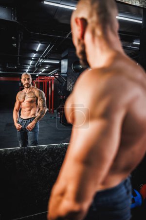 Foto de Foto de un joven fitness posando después de hacer ejercicio en el gimnasio y mostrando sus músculos perfectos frente a un espejo. - Imagen libre de derechos