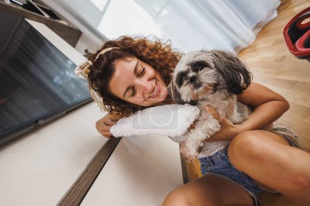 Foto de Joven mujer sonriente divirtiéndose con su perro mascota mientras hace sus tareas diarias en casa. - Imagen libre de derechos