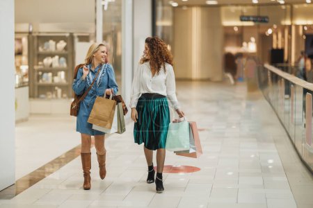 Téléchargez les photos : Tourné de deux belles femmes souriantes portant des sacs et profitant d'une journée de shopping dans un centre commercial de la ville. - en image libre de droit
