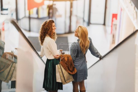 Téléchargez les photos : Tourné de deux jolies femmes souriantes qui prennent un peu de temps pour profiter d'une virée shopping dans le centre commercial de la ville. - en image libre de droit