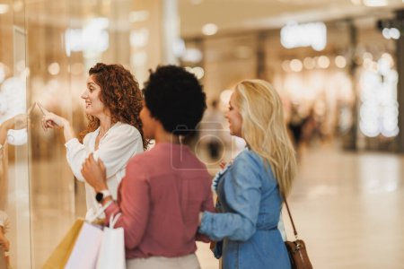 Téléchargez les photos : Une jolie femme pointant vers quelque chose tout en profitant d'une journée de shopping avec ses meilleurs amis dans le centre commercial de la ville. - en image libre de droit