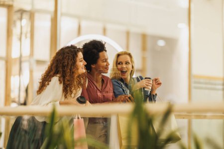 Foto de Tiro de tres mujeres atractivas divirtiéndose y hablando en un centro comercial juntos mientras están fuera en una juerga de compras. - Imagen libre de derechos