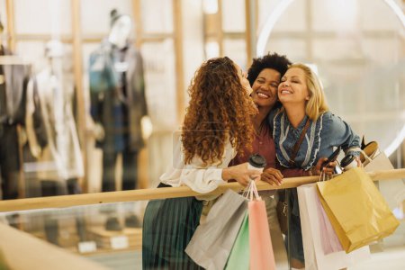 Téléchargez les photos : Plan recadré de trois jolies femmes joyeux collant ensemble lors d'une séance de shopping dans le centre commercial de la ville. - en image libre de droit
