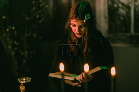 Foto de Retrato de una linda adolescente que está leyendo un gran libro viejo y preparándose para la fiesta de Halloween. - Imagen libre de derechos