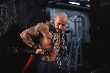 Photo for Shot of a young fitness man standing in the gym and preparing to strength training with heavy chain around his neck. - Royalty Free Image