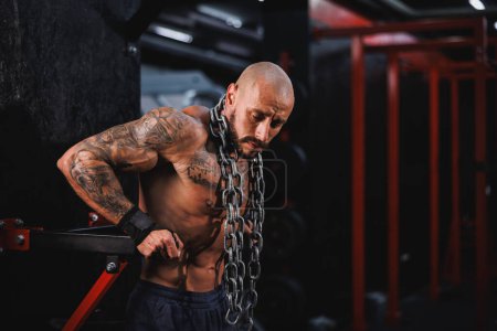 Photo for Shot of an athletic young man working out with a heavy chain around his neck in the gym. - Royalty Free Image