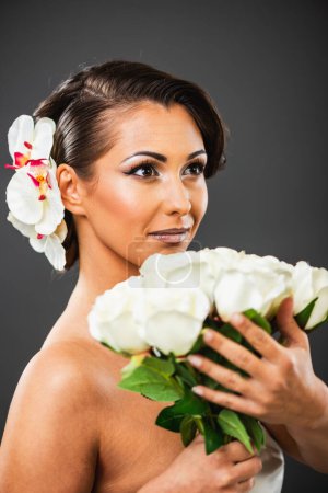 Foto de Retrato de una atractiva joven con un bonito maquillaje y un ramo de rosas blancas posando en un estudio sobre fondo oscuro. - Imagen libre de derechos