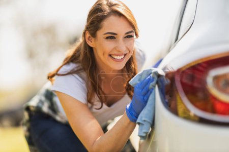 Photo for A smiling young woman with protective gloves wipes her car with a cloth ready to hit the road. - Royalty Free Image