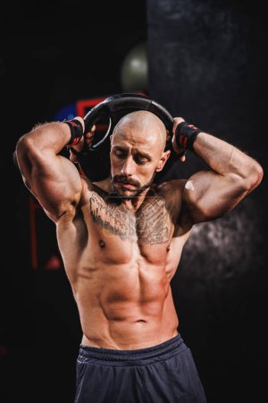 Téléchargez les photos : Prise de vue d'un bodybuilder musculaire montrant ses muscles parfaits après avoir travaillé avec la plaque de poids à la salle de gym. - en image libre de droit