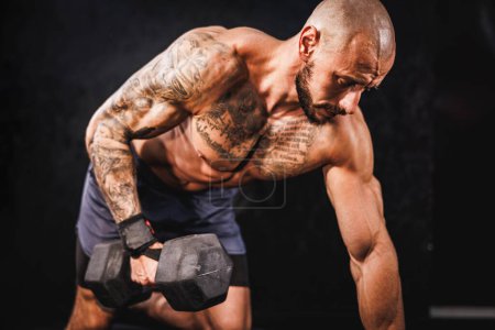 Foto de Una foto de un musculoso fisicoculturista haciendo entrenamiento duro con mancuerna en el gimnasio. Él está bombeando su músculo bíceps con peso pesado. - Imagen libre de derechos