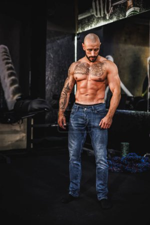 Foto de Foto de un joven musculoso culturista mostrando sus músculos perfectos mientras posaba en el gimnasio. - Imagen libre de derechos