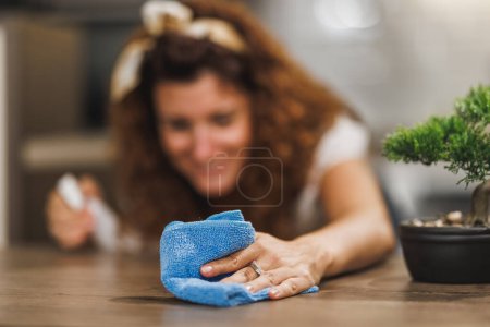 Foto de Primer plano de la mano de una mujer haciendo sus tareas diarias en casa. Ella está limpiando y desinfectando la superficie con un trapo y spray. - Imagen libre de derechos