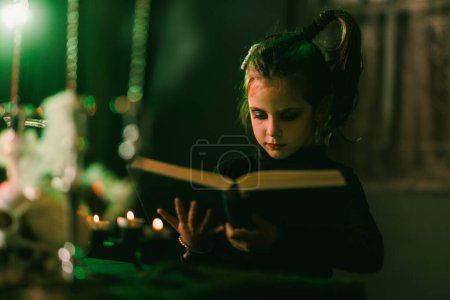 Foto de Retrato de una linda niña que está leyendo un gran libro viejo y preparándose para Halloween. - Imagen libre de derechos