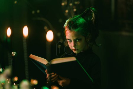 Foto de Retrato de una linda niña está sosteniendo un gran libro viejo y preparándose para Halloween. Mirando la cámara. - Imagen libre de derechos