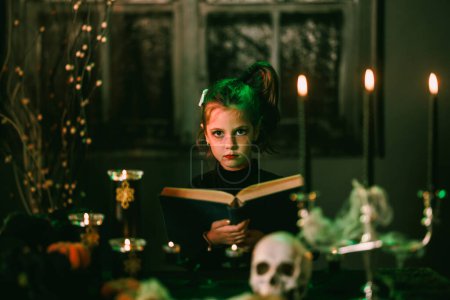 Téléchargez les photos : Portrait d'une mignonne petite fille d'Halloween avec un énorme vieux livre. Regardant la caméra. - en image libre de droit