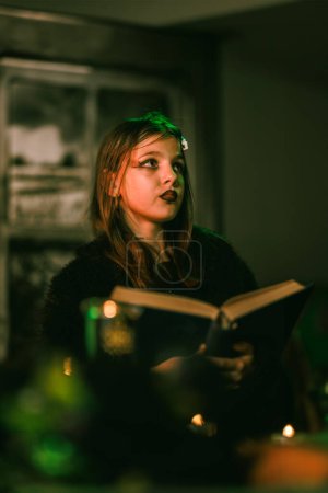 Foto de Retrato de una linda chica con un enorme libro viejo que se está preparando para la fiesta de Halloween. - Imagen libre de derechos