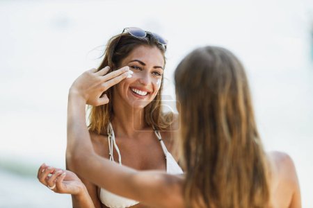 Téléchargez les photos : Adolescente s'amuse avec sa jeune mère sur la plage. Ils appliquent de la lotion solaire tout en profitant de vacances d'été. - en image libre de droit