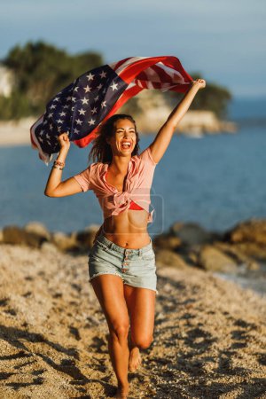 Foto de Attractive young woman with American national flag having fun and spending the day on the beach. - Imagen libre de derechos