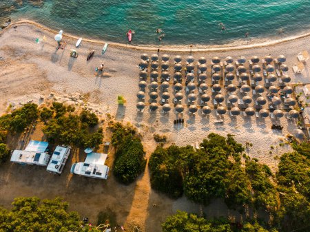 Luftaufnahme des erstaunlichen idyllischen Strandes mit Schilfschirmen und Menschen, die sich entspannen und bei sonnigem Wetter im klaren Wasser des Mittelmeeres schwimmen.