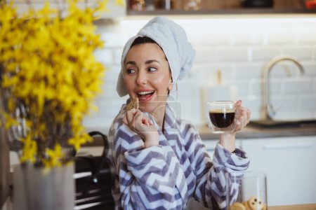 Foto de Una joven atractiva disfrutando de un café de la mañana y galletas en su cocina en casa. - Imagen libre de derechos