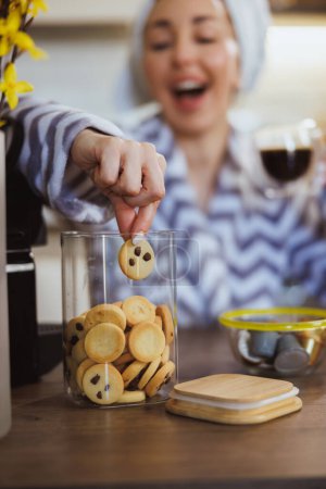 Foto de Mujer joven comiendo galletas frescas caseras y disfrutando del café de la mañana en casa. - Imagen libre de derechos