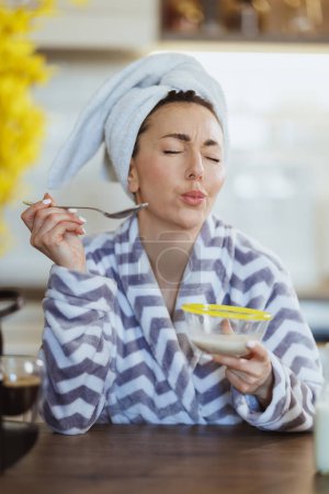 Téléchargez les photos : Une jolie jeune femme en peignoir préparant une avoine instantanée pour le petit déjeuner et ayant rituel de plaisir matinal à la maison. - en image libre de droit