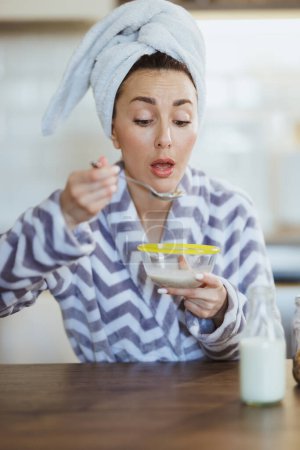 Foto de Mujer joven en albornoz comiendo avena instantánea para el desayuno en la cocina en casa. - Imagen libre de derechos